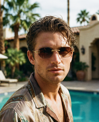 Man wearing cossino luxury sunglasses with a pool and palm trees in the background
